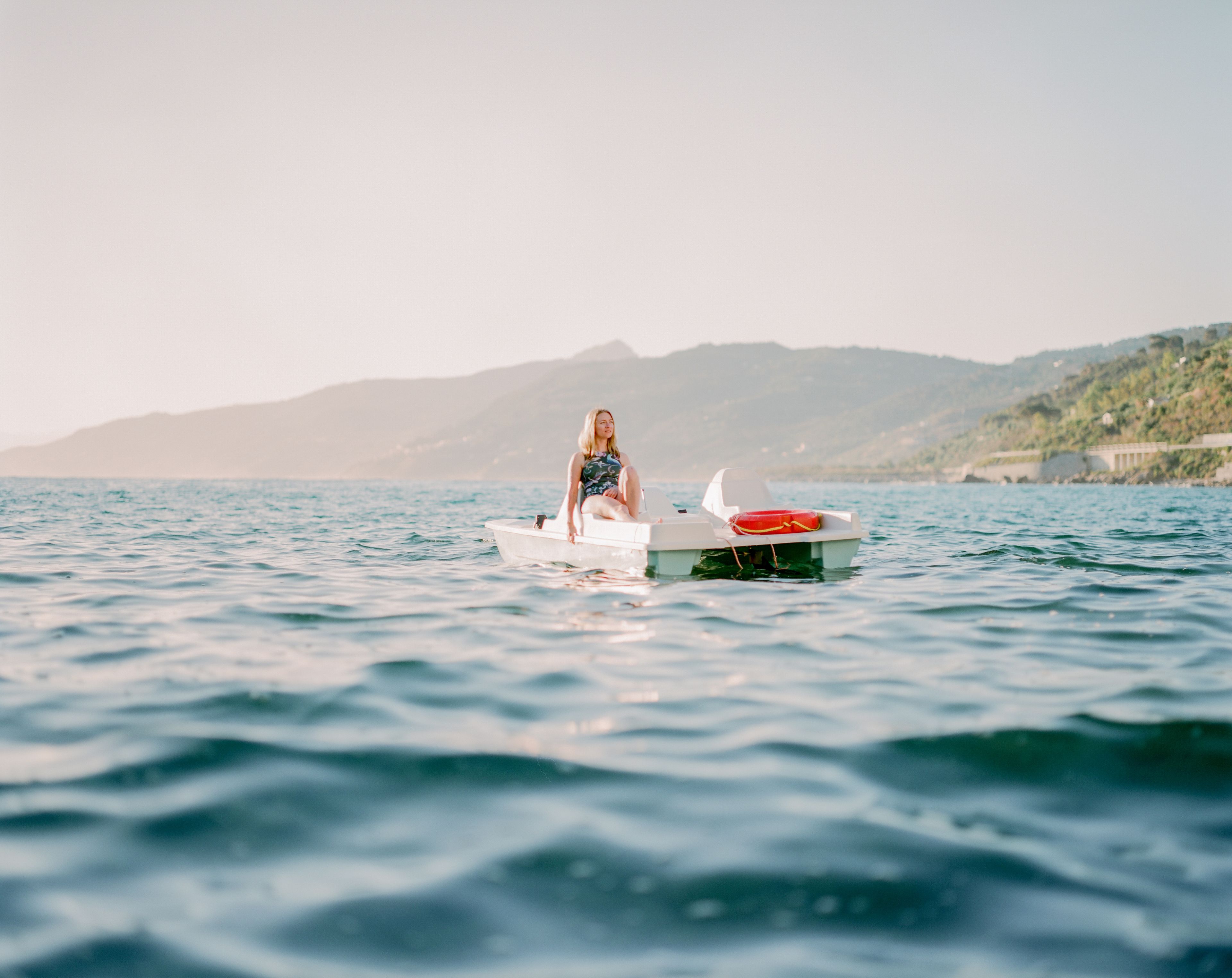 A person sitting on a small boat in calm water with a mountainous landscape in the background.