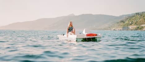 Una persona sentada en un pequeño bote en aguas tranquilas, con un paisaje montañoso al fondo.
