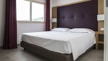 A modern hotel room with a large bed, a wooden headboard, two bedside lamps, and a window with curtains.