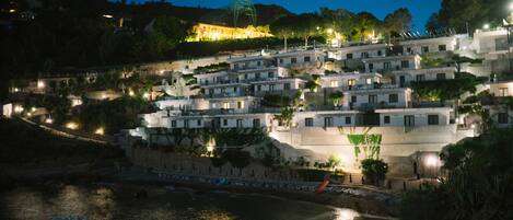 A coastal village with terraced buildings, a waterfront, and a hilltop structure.