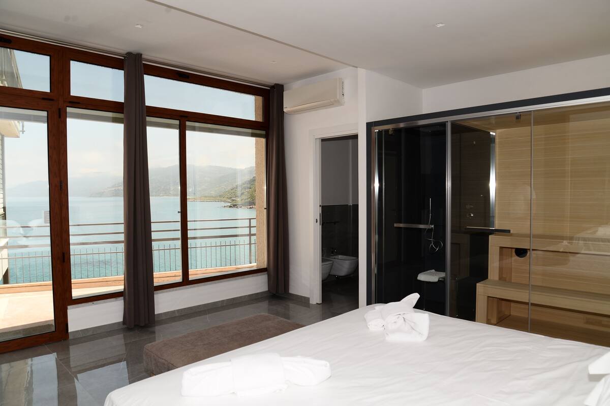 A modern hotel room with a large sliding glass door to a balcony overlooking a body of water and mountains.
