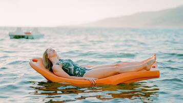 Une personne allongée sur un flotteur orange dans une eau calme, avec un bateau visible à l’arrière-plan.