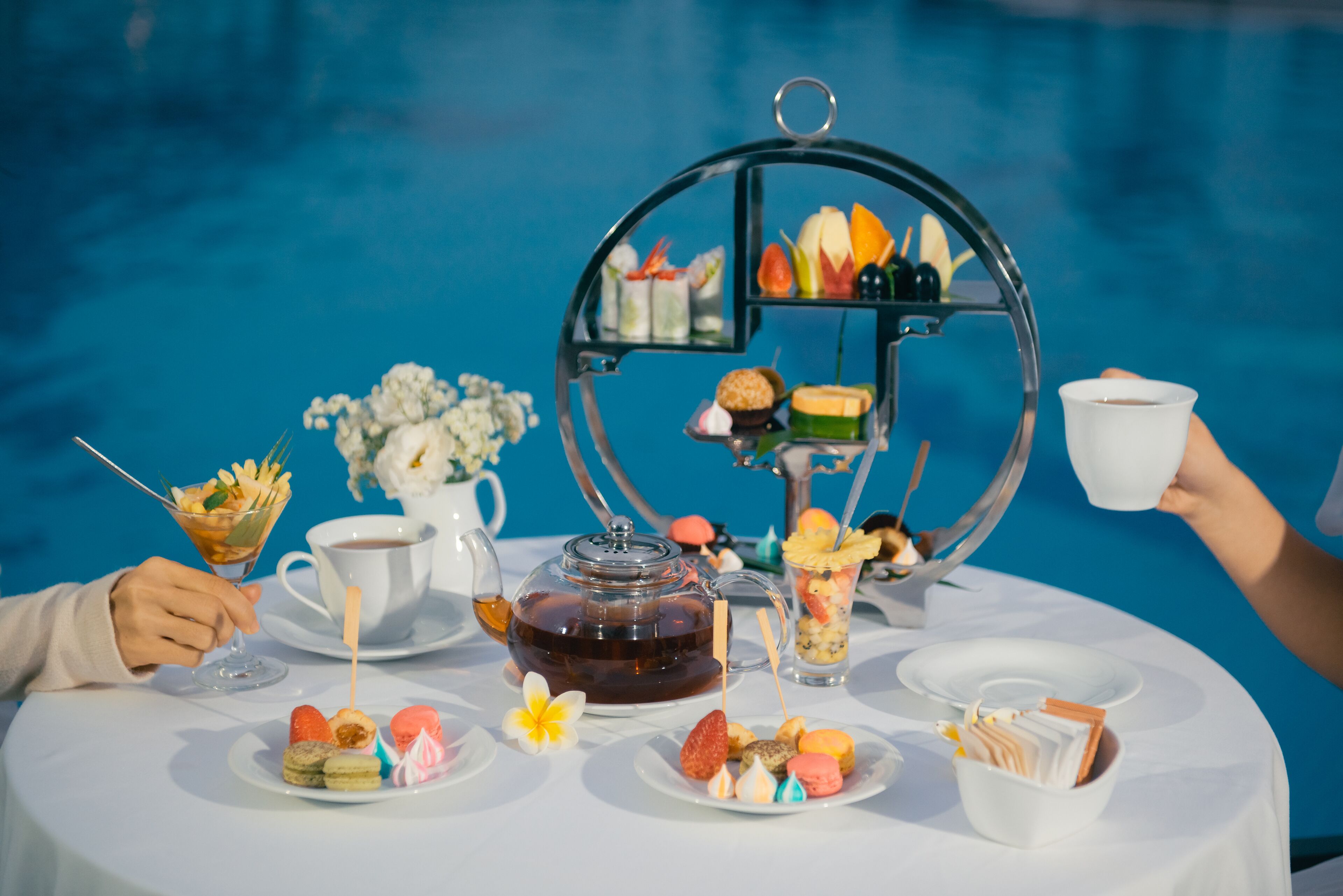 A table with a variety of food and drinks, including a teapot, a cup, and a tray with snacks and desserts.