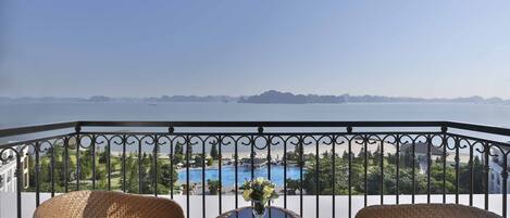 Varanda com cadeiras de vime e uma mesa, com vista para uma piscina e montanhas ao longe.