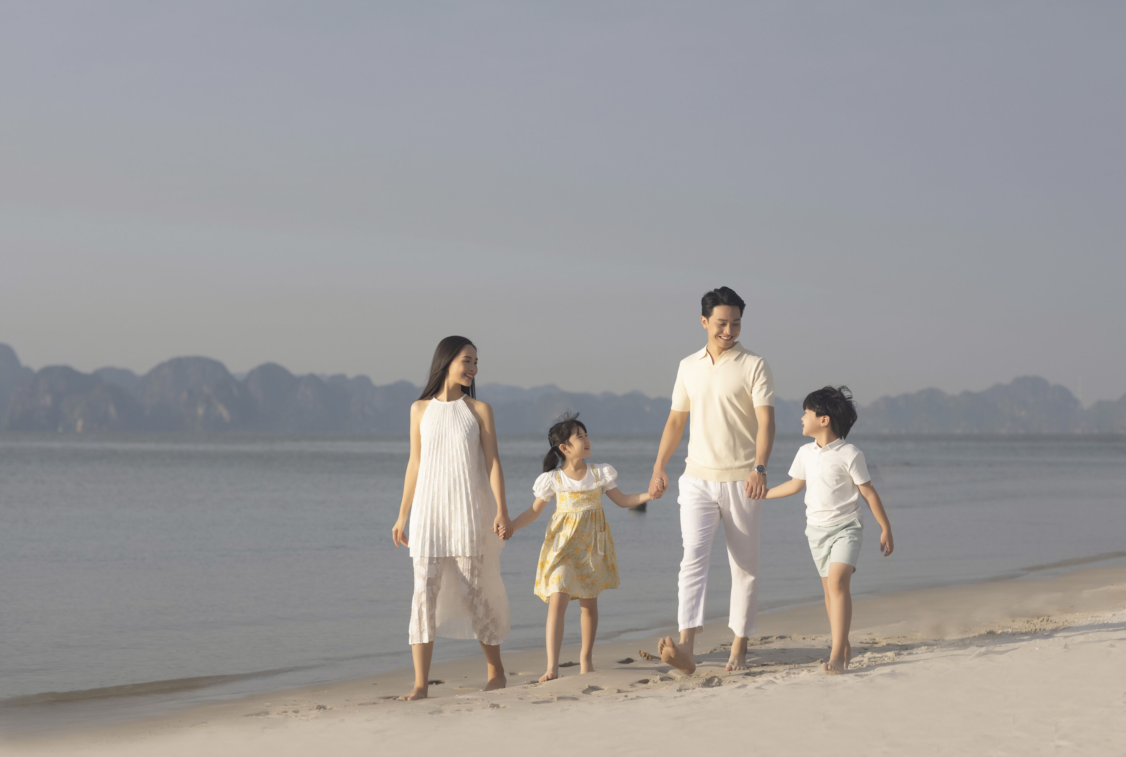 A family walking on a beach with a calm sea and distant mountains in the background.