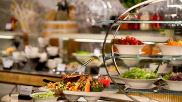 A buffet with various food options including salads, fruits, and a meat dish.