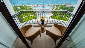 A balcony with wicker chairs and a table with a vase of flowers, overlooking a pool and a coastal view. - Vinpearl Resort & Spa Ha Long  (Bai Chay)