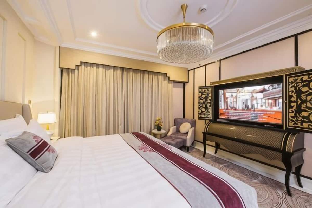 A hotel room with a large bed, a television, a chair, and a decorative wall panel.