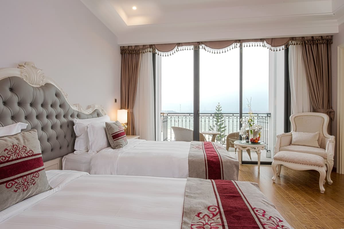 A hotel room with two beds, a balcony with a view, and a chair.