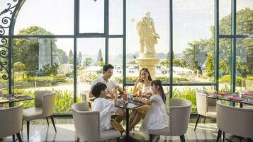 A group of people dining at a table with a view of a statue and greenery outside.