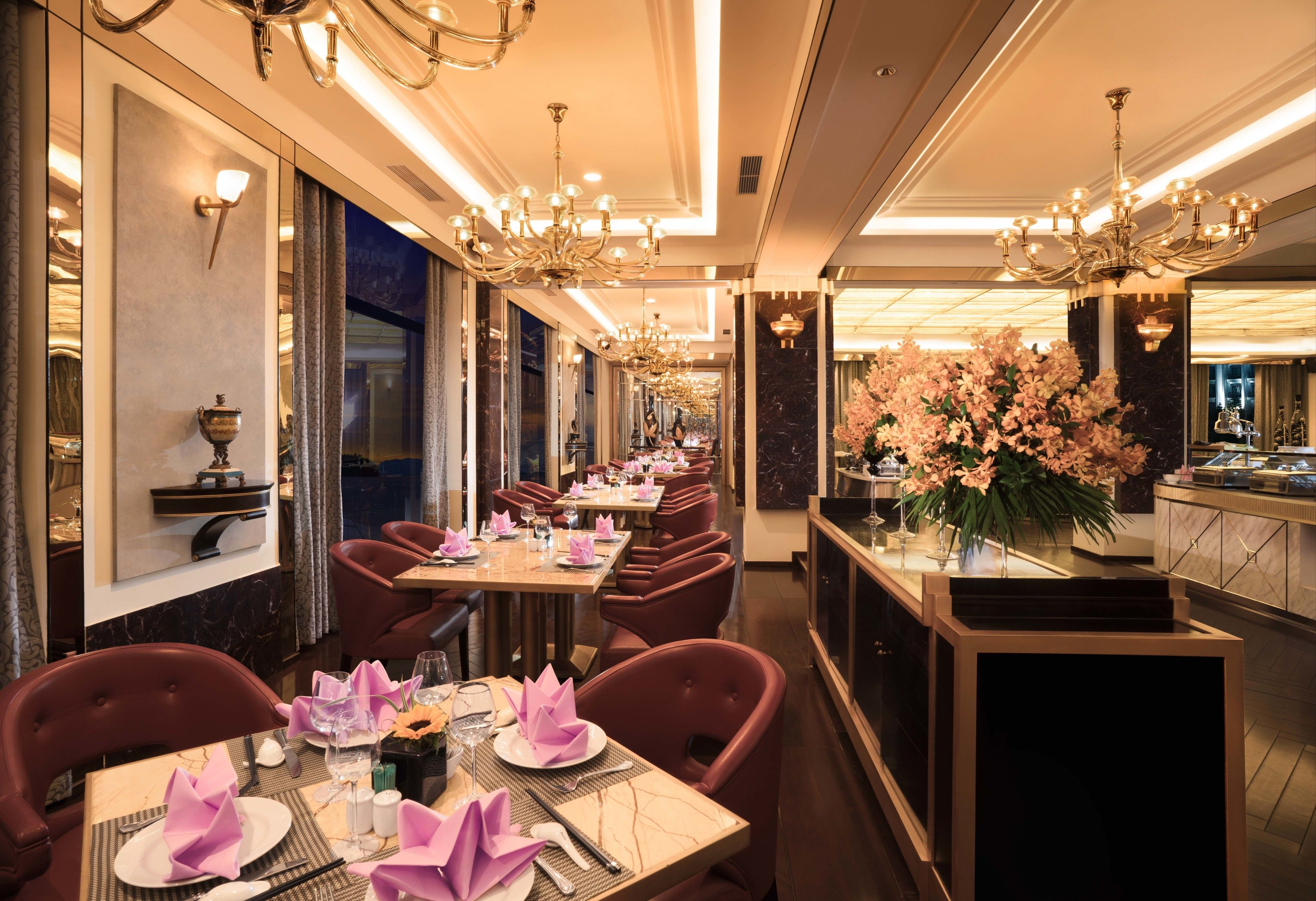 A restaurant with marble-topped tables, red upholstered chairs, and chandeliers.