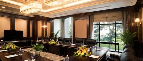 Un salón de conferencias con una mesa larga, sillas, un televisor y vistas al exterior.