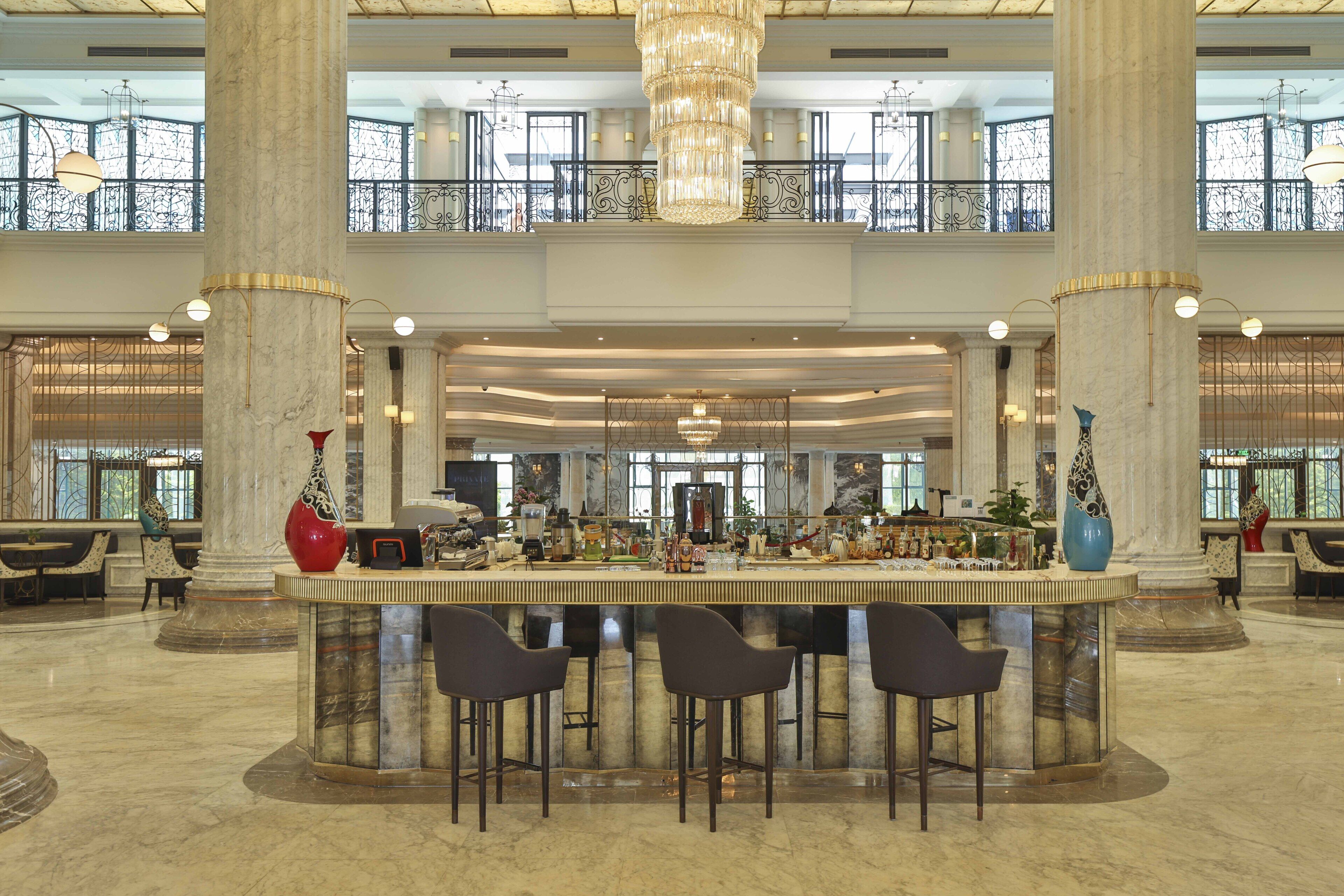 Eine großzügige Lobby mit einer zentralen Bar, hohen Decken und großen Säulen.