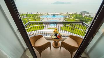A balcony with wicker chairs, a small table with a vase of flowers, and a view of a swimming pool and beach.