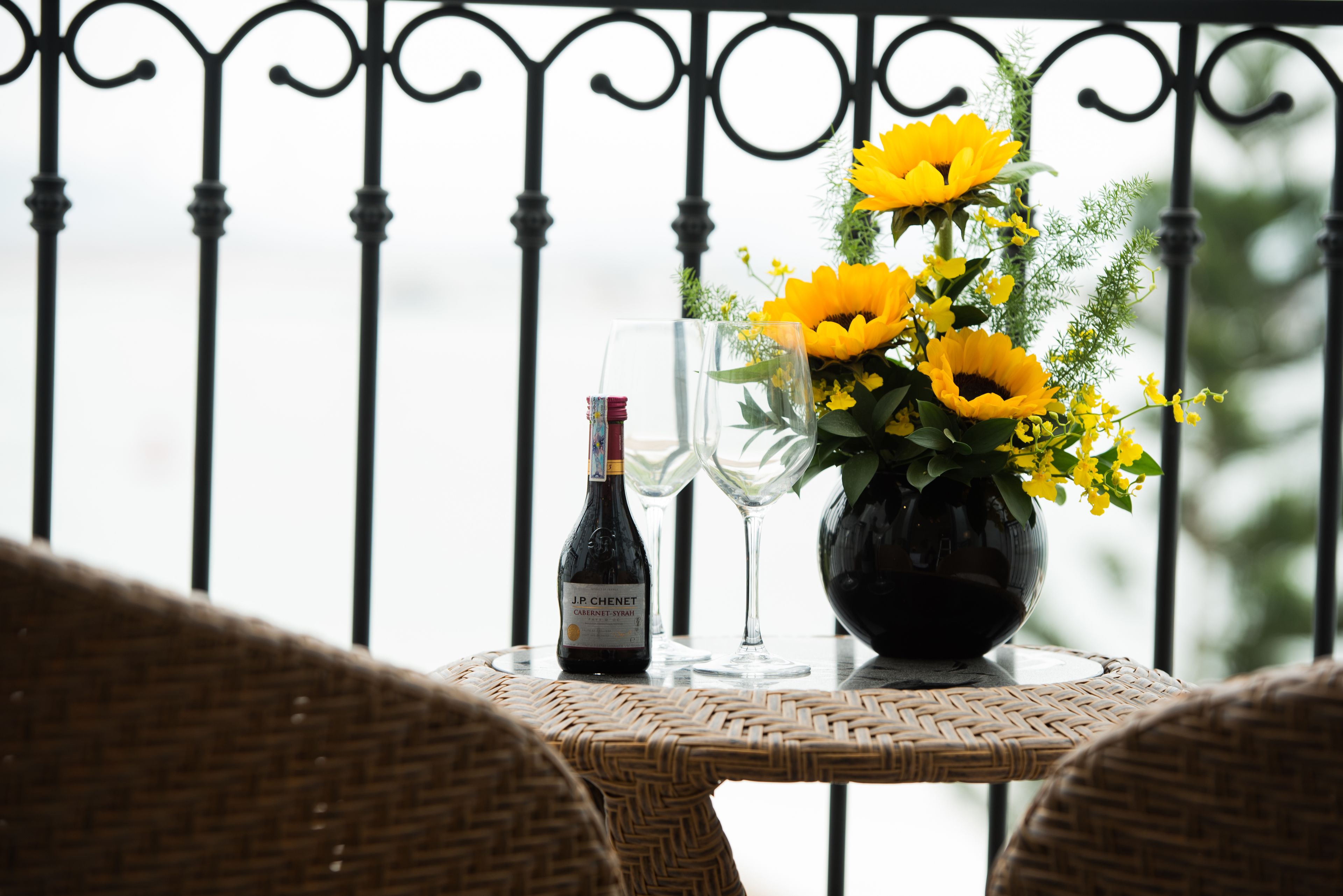 A table with a bottle of wine, two glasses, and a vase with yellow flowers.