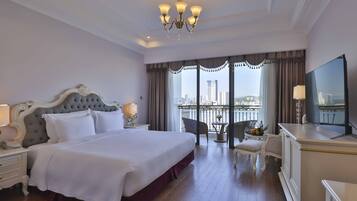 A hotel room with a large bed, a TV, a desk, and a balcony with a city view.