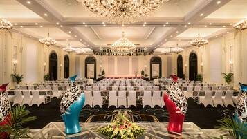 Un salón de banquetes con varias mesas, candelabros y un escenario.