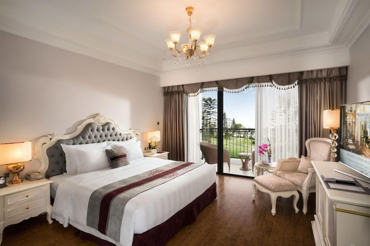 A hotel room with a large bed, a chandelier, a desk, and a view of the outdoors.