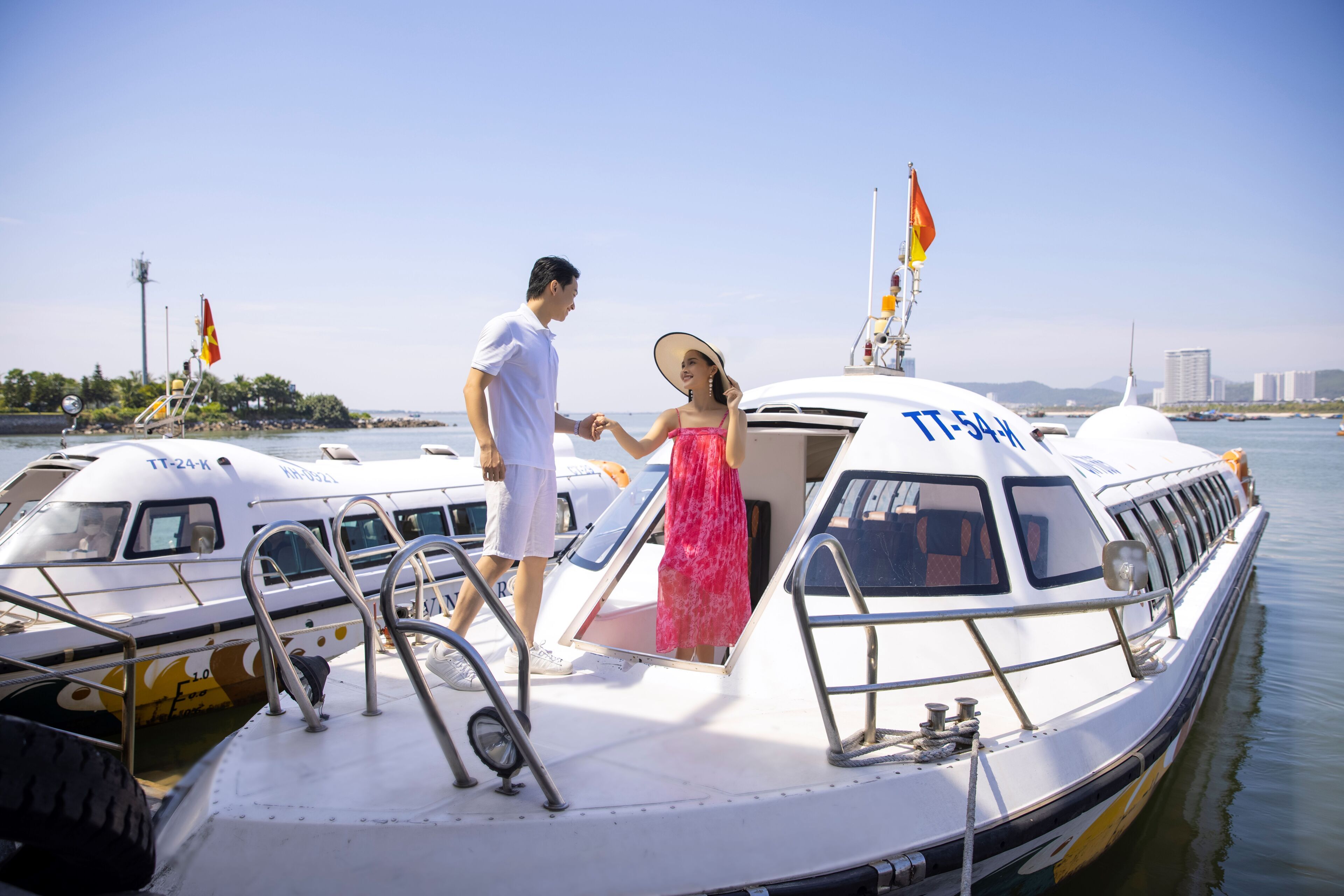 A boat docked at a marina with a clear view of the water and a city skyline in the background.