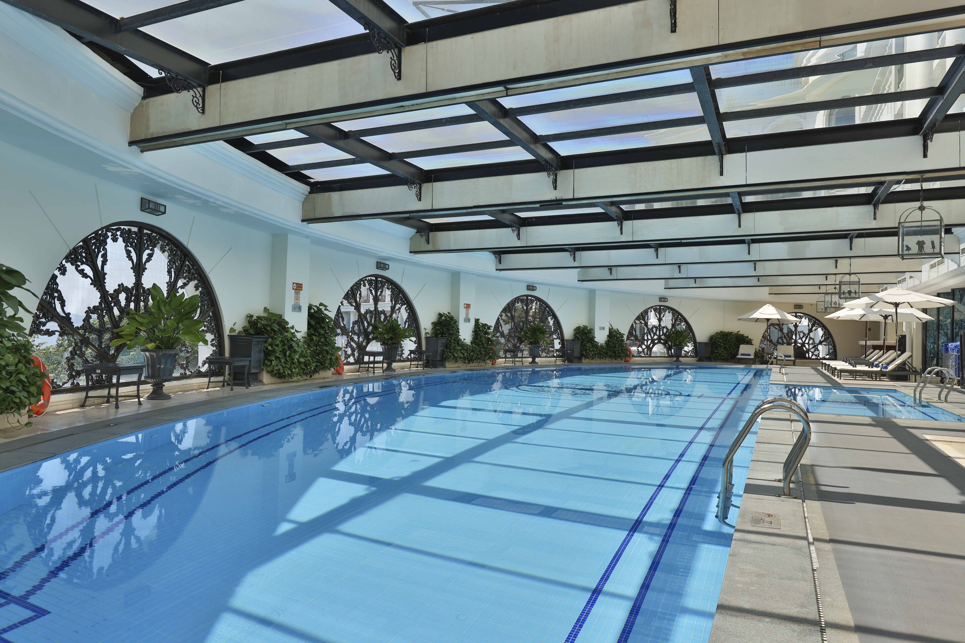 An indoor swimming pool with clear blue water, surrounded by lounge chairs and potted plants.