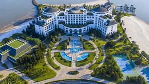 A large, white, multi-story hotel with a central courtyard, surrounded by water and a beach. - Vinpearl Resort & Spa Ha Long  (Bai Chay)