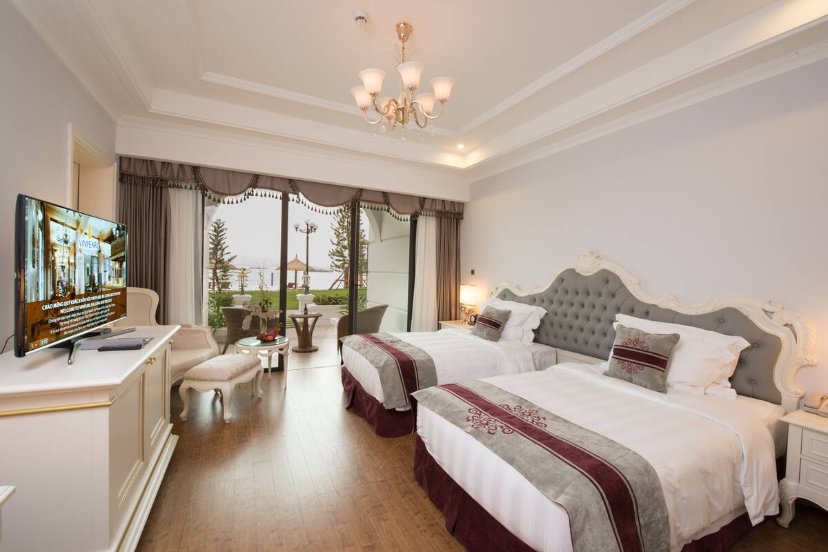 A hotel room with two beds, a TV, a desk, and a view of the outdoors.