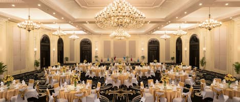 A banquet hall with round tables, white chairs, and gold accents.
