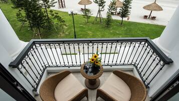 A balcony with wicker chairs and a table with a vase of sunflowers, overlooking a beach with umbrellas and lounge chairs.