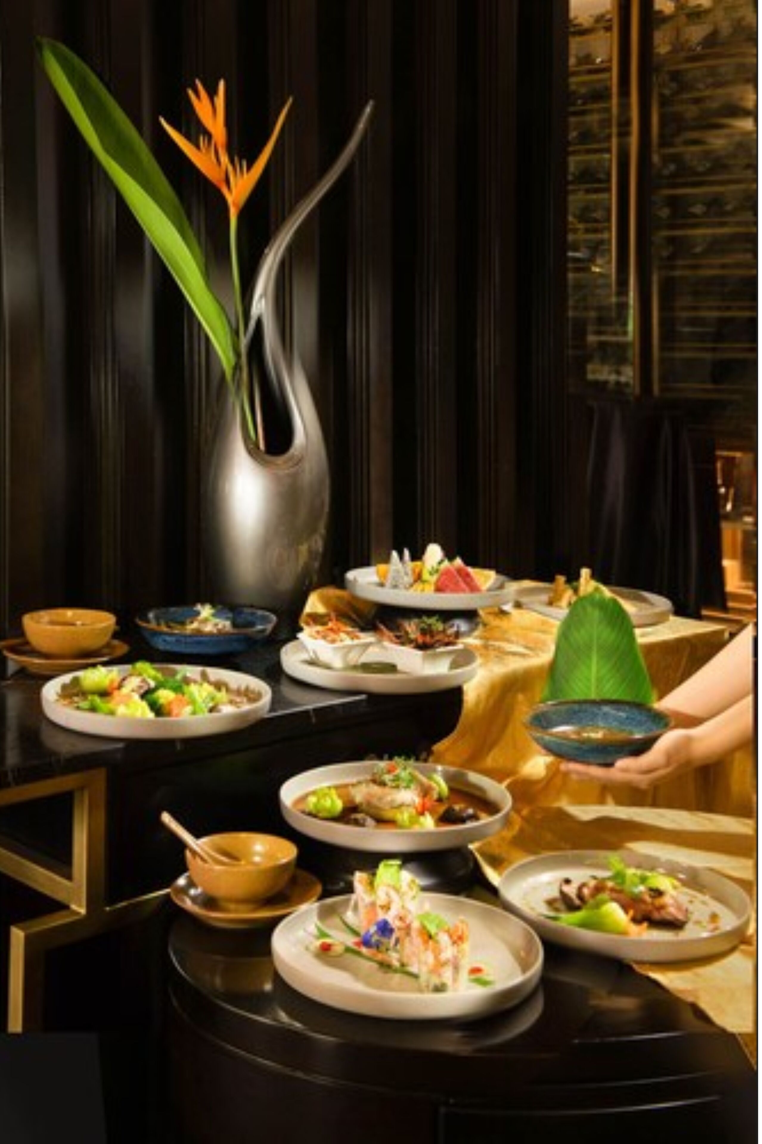 A dining table set with various dishes, a vase with a plant, and a person holding a bowl.