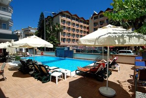 A swimming pool with lounge chairs and umbrellas, surrounded by a multi-story building with balconies. - Hatipoglu Beach Hotel (Alanya)