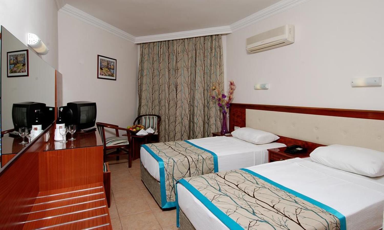 A hotel room with two beds, a desk with a computer and a chair, a mirror, and a window with curtains.