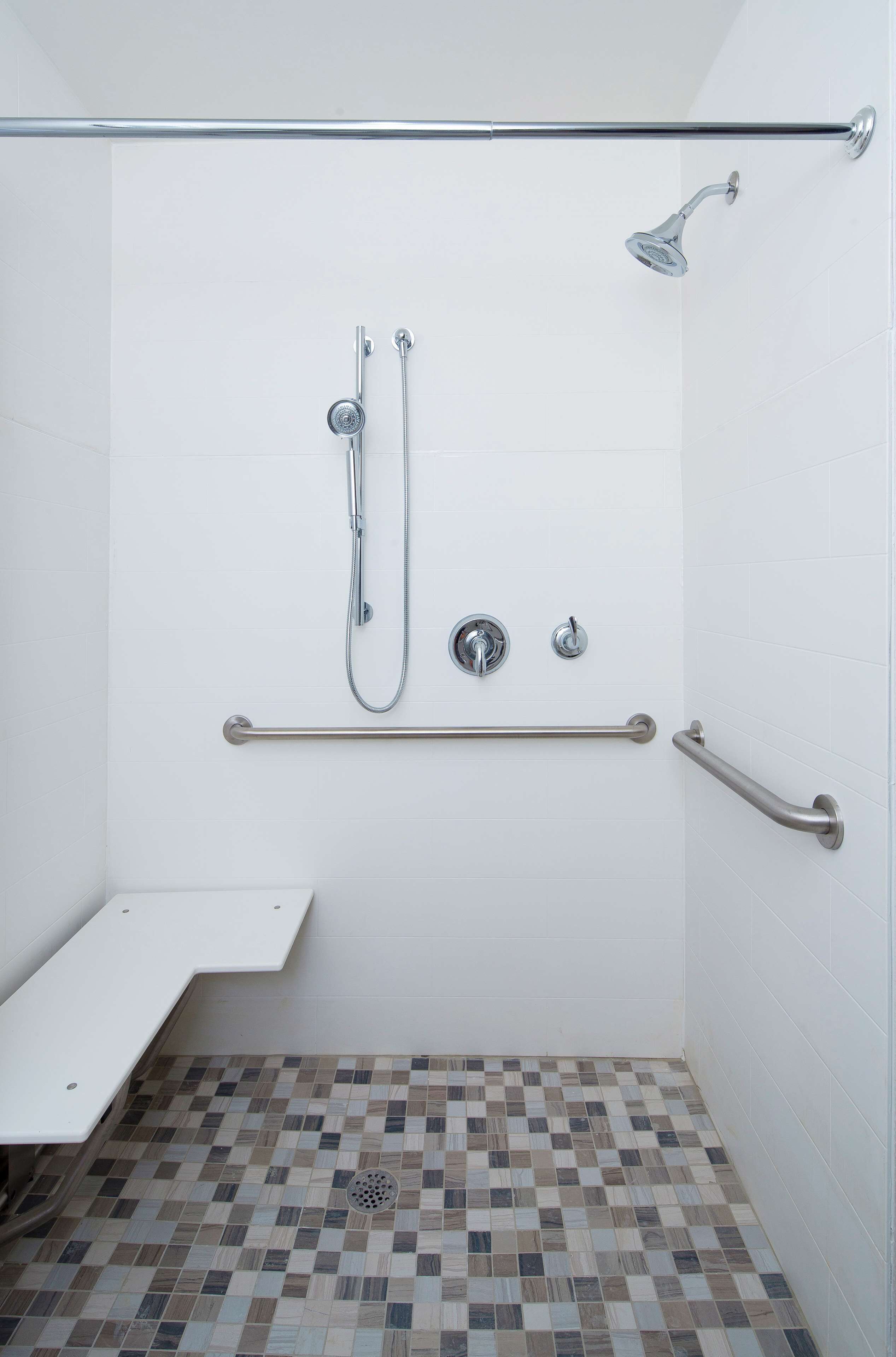 A shower area with a grab bar, a handheld showerhead, and a wall-mounted faucet.