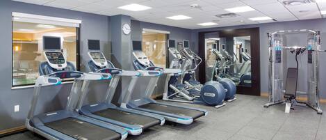 Un gimnasio con cintas de correr, elípticas y equipo de pesas.