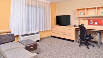 A hotel room with a bed, a desk with a computer and phone, a chair, and a TV.