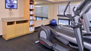 Un gimnasio con cintas de correr, una bicicleta estática y una pelota de ejercicios azul. Hay un mueble de madera con toallas y un teléfono en la pared.