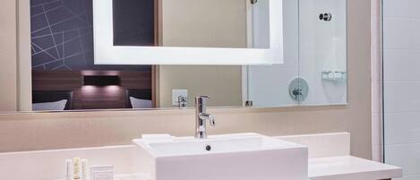Une salle de bain moderne avec un grand miroir, un lavabo blanc et une douche à parois de verre.