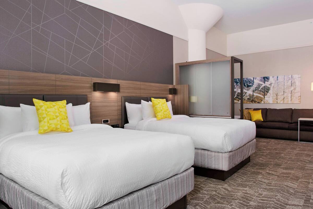 A hotel room with two beds, a sofa, and a large window.