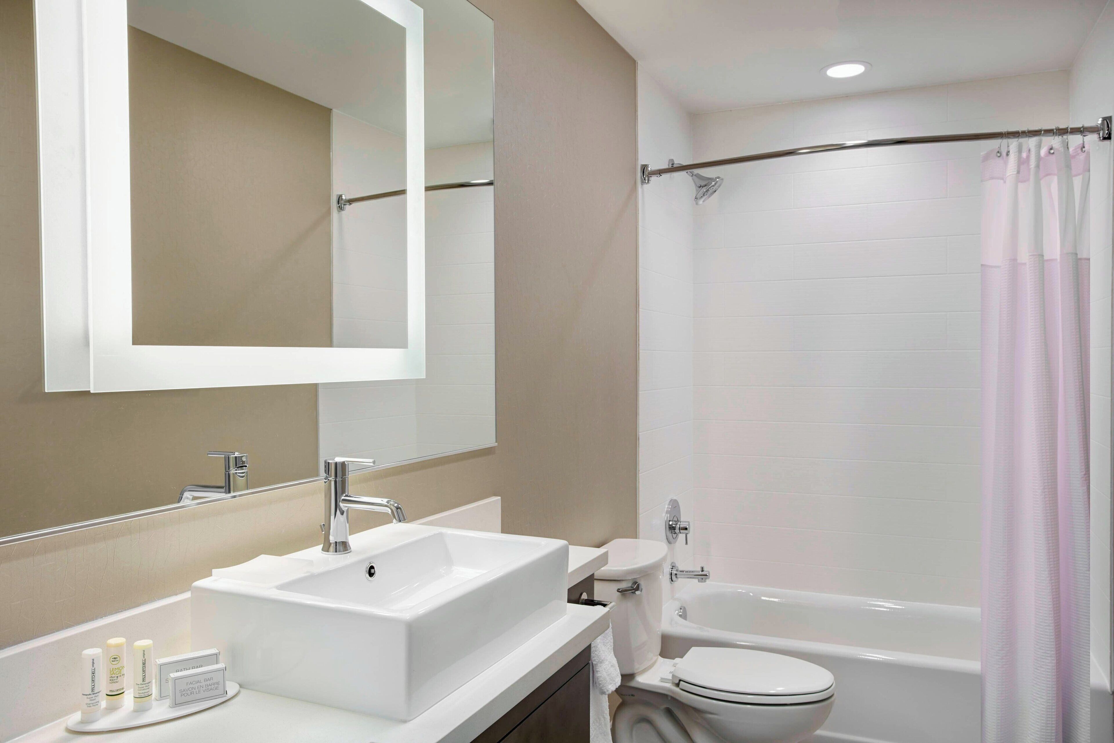 A modern bathroom with a white sink, mirror, toilet, and bathtub.