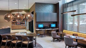 A modern hotel lobby with hexagonal pendant lights, a reception desk, seating areas, and a large window with a view. - SpringHill Suites by Marriott Milwaukee Downtown (Milwaukee)