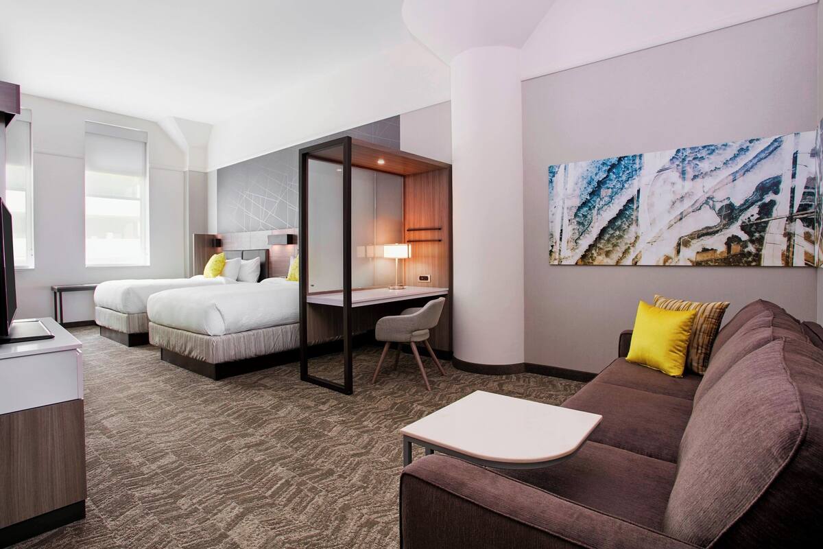 A hotel room with two beds, a desk, a couch, and a large abstract painting on the wall.