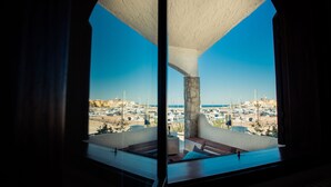 Uitzicht vanaf een balkon met een helderblauwe lucht, een stenen pilaar en een jachthaven met boten.