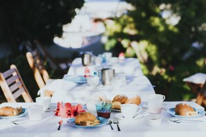 A table set for breakfast with croissants, coffee cups, and a flower arrangement. - B&B Sa Cruxitta (Portoscuso)