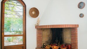 Een hoekzaal met een haard van baksteen, een houten deur met een metalen rooster en een witte muur met twee ronde decoraties.