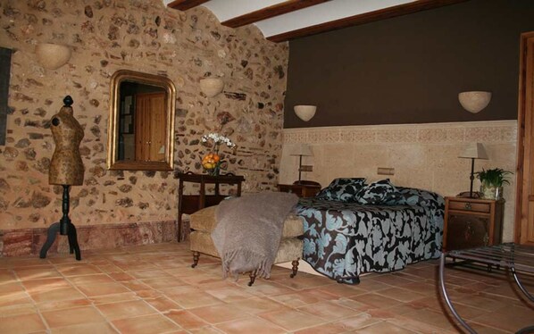 Um quarto rústico com parede de pedra, cama com roupa de cama estampada, cômoda de madeira e um espelho.