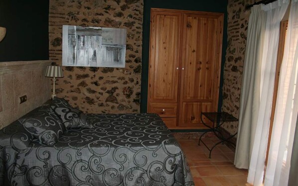 A bedroom with a bed, a wooden wardrobe, a small table, and a lamp. - Hotel Casa Babel (Villalonga)