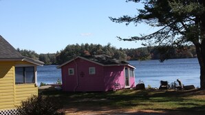 A pink cabin with a small porch and a view of a lake.