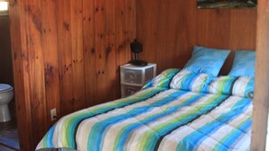 A wooden-paneled room with a bed, a nightstand, and a painting on the wall.