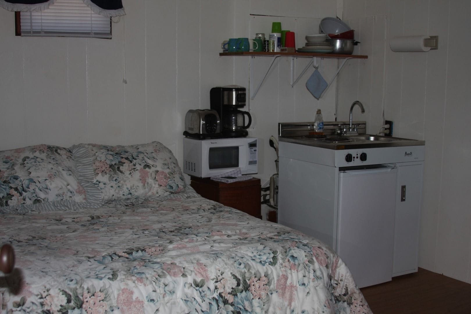A small, compact room with a bed, a kitchenette with a microwave, a stove, and a sink.