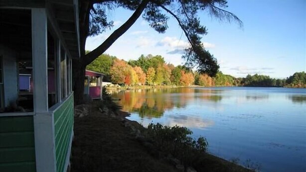 A lakeside cabin with a view of a calm lake and autumn foliage.