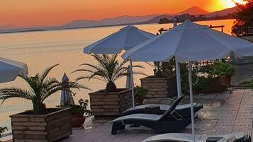 Una zona relax vista mare con lettini e ombrelloni, affacciata su un'acqua calma e un tramonto.
